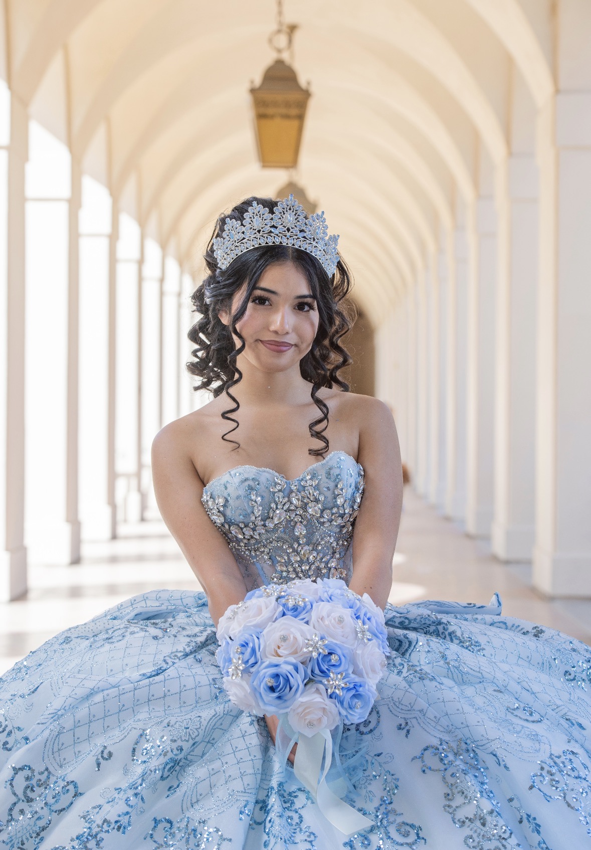 Quinceañera in a blue beaded gown holding a bouquet